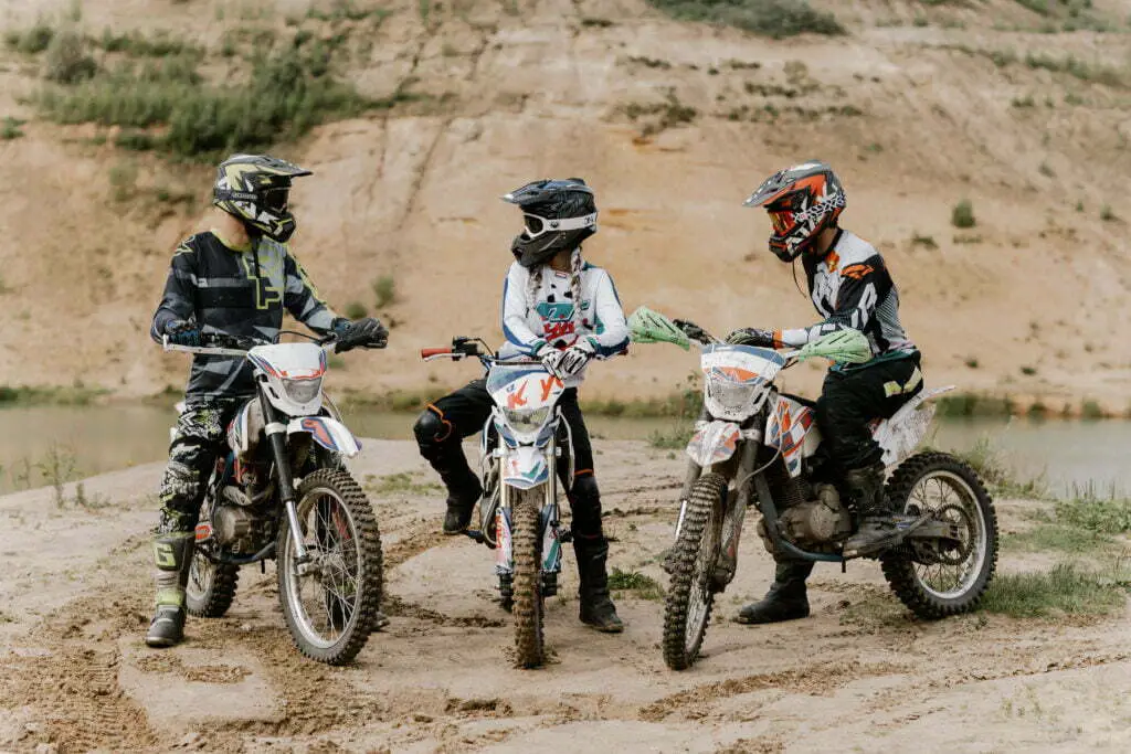 three young people standing with dirt bikes